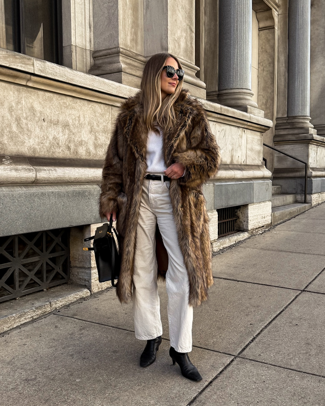 Textured dark faux-fur coat with an ivory sweater, white trousers and black boots