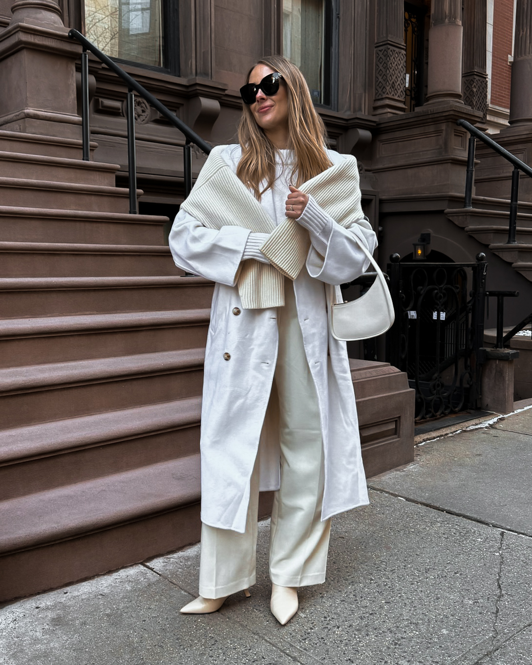 White winter coat over cream knitwear, white trousers and light pointed boots