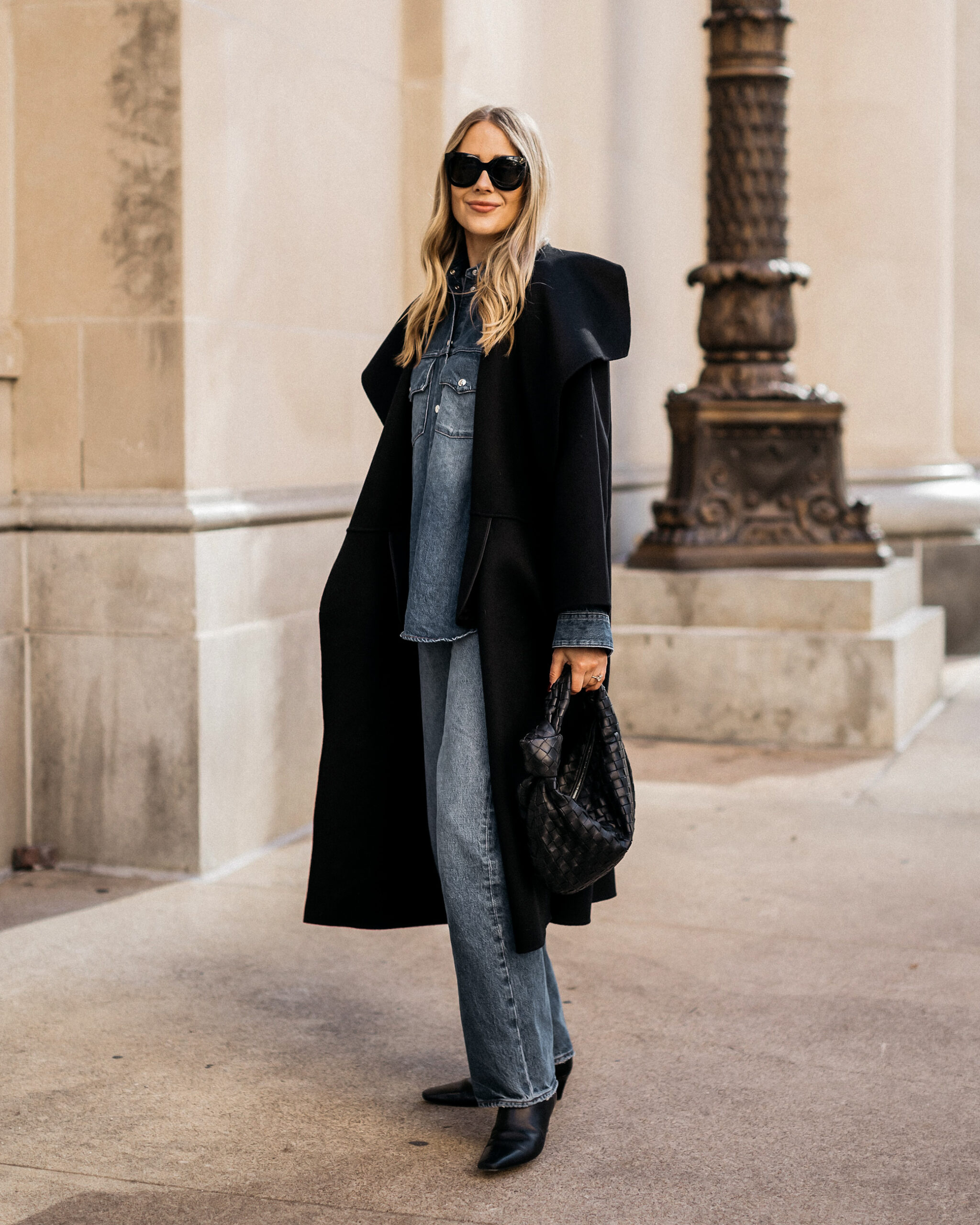 Long black coat over a blue denim shirt and jeans with black pointed boots