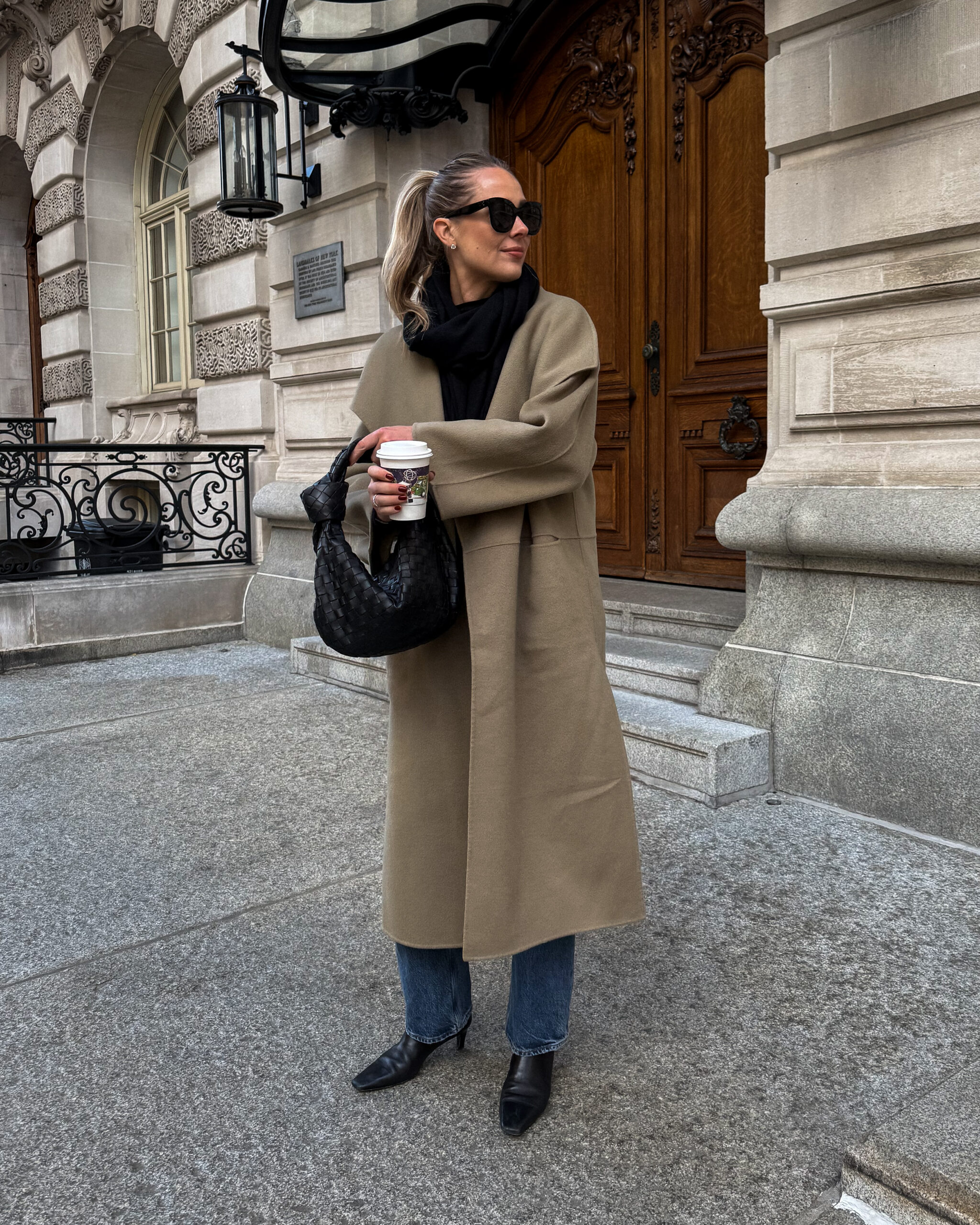 Long camel coat with a black scarf, blue jeans and black ankle boots